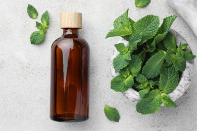 Photo of Bottle of essential oil and mint on light textured table, flat lay