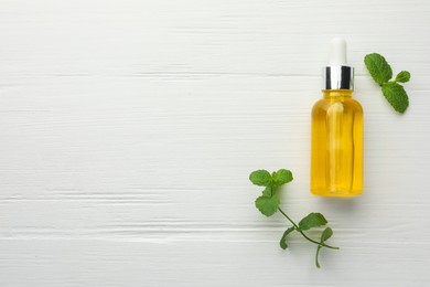 Photo of Bottle of essential oil and mint on white wooden table, flat lay. Space for text