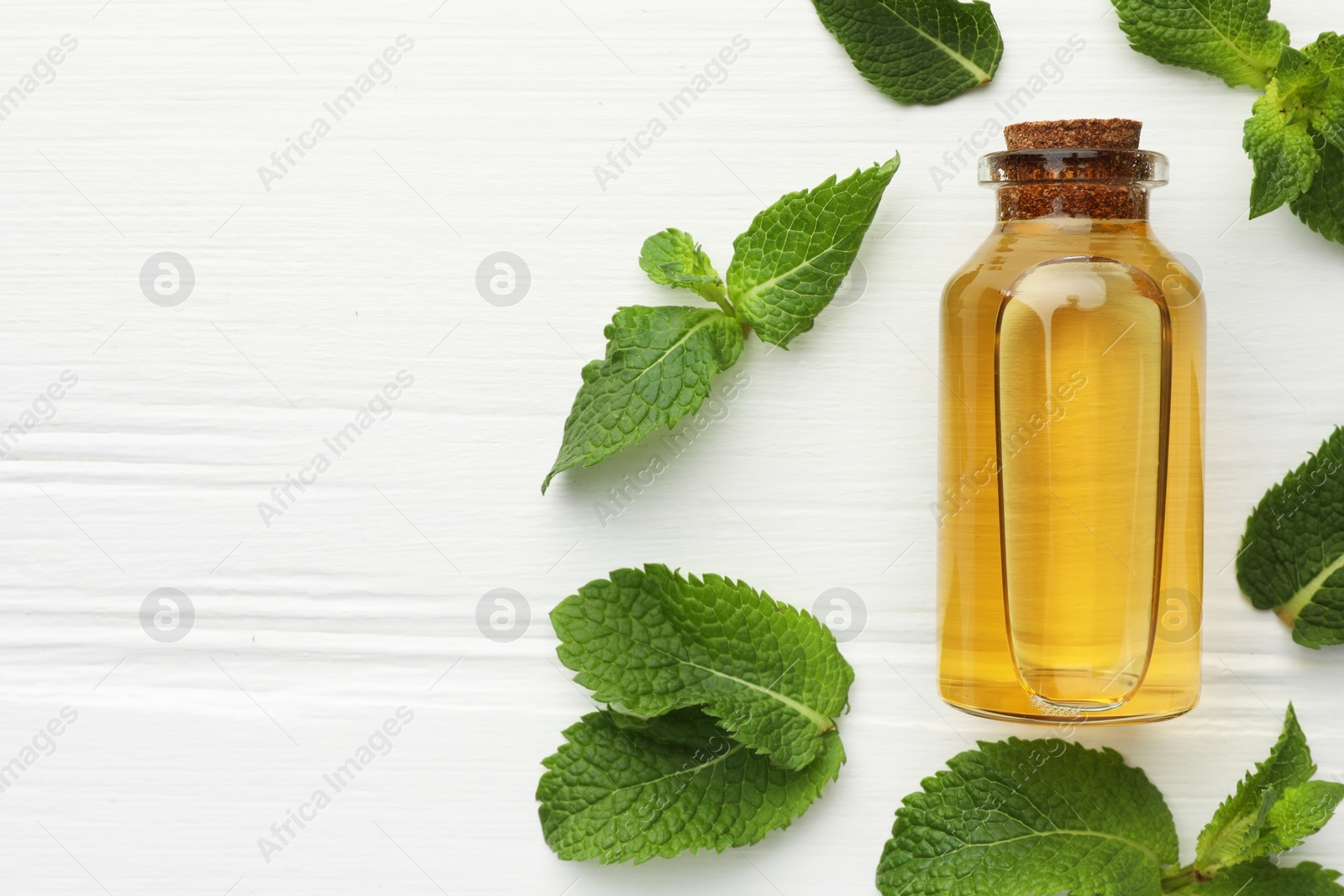 Photo of Bottle of essential oil and mint on white wooden table, flat lay. Space for text