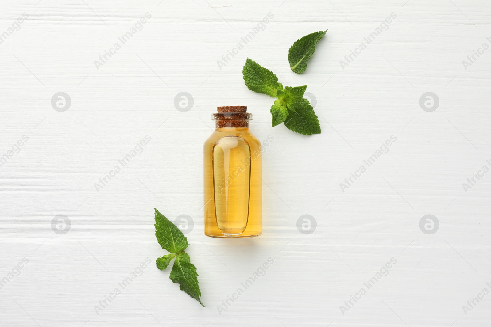 Photo of Bottle of essential oil and mint on white wooden table, flat lay