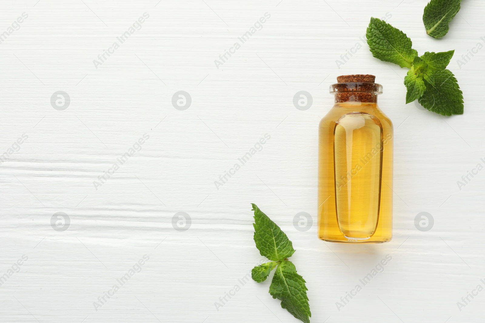 Photo of Bottle of essential oil and mint on white wooden table, flat lay. Space for text