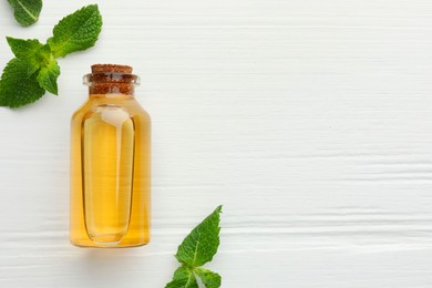 Photo of Bottle of essential oil and mint on white wooden table, flat lay. Space for text