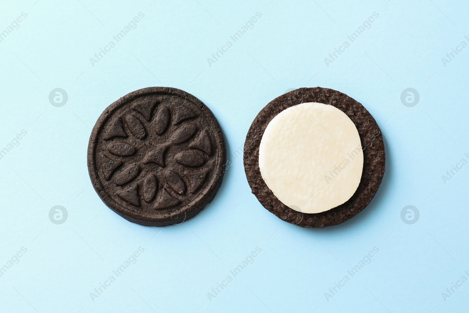 Photo of Halves of tasty sandwich cookie on light blue background, top view