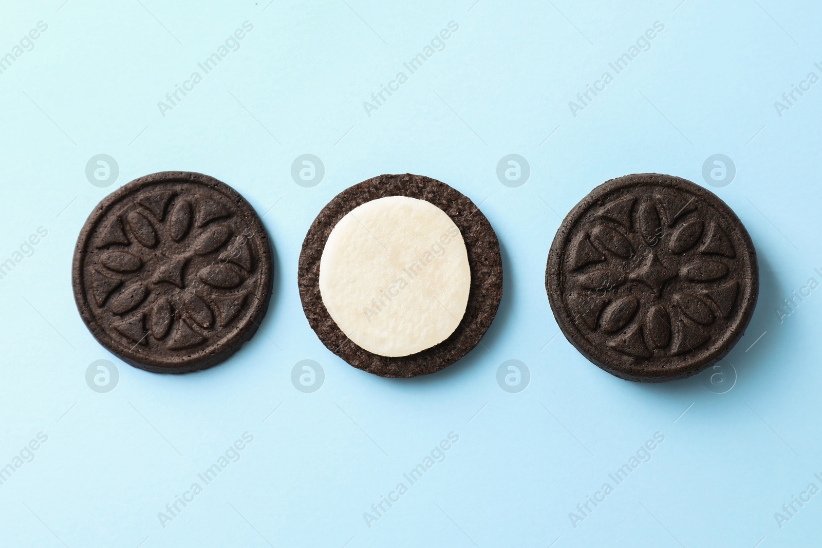 Photo of Tasty sandwich cookies with cream on light blue background, top view