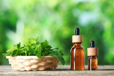 Photo of Bottles of mint essential oil and fresh leaves on wooden table