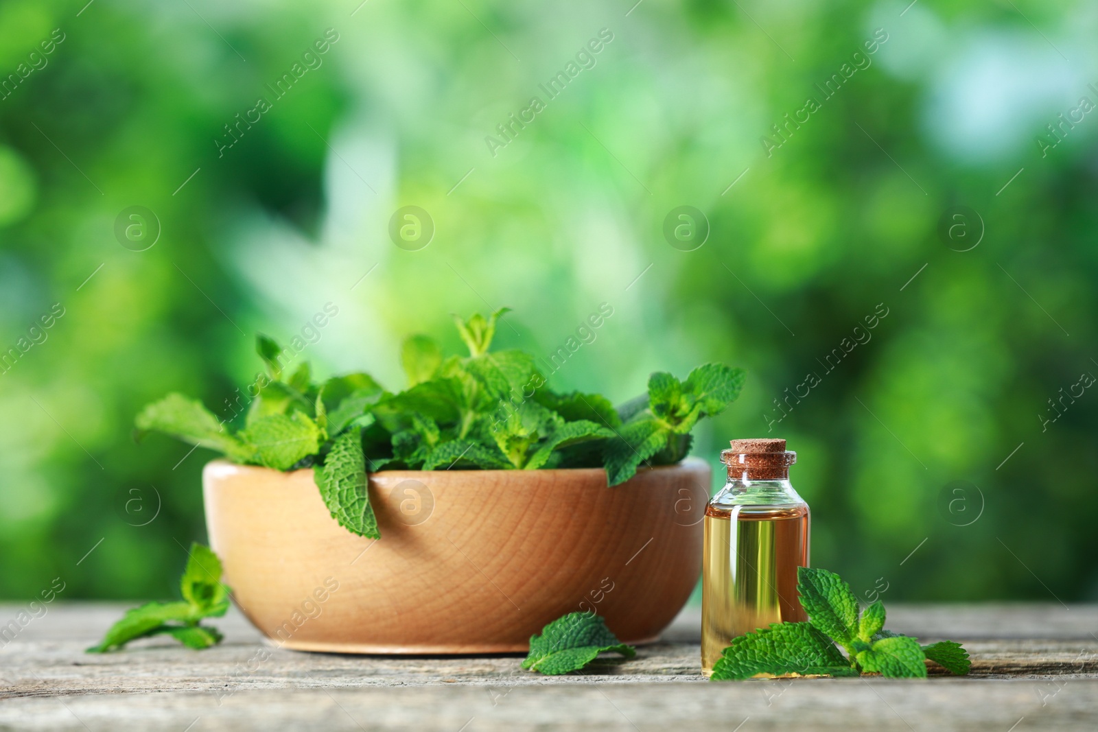 Photo of Bottle of mint essential oil and fresh leaves on wooden table