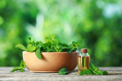 Photo of Bottle of mint essential oil and fresh leaves on wooden table