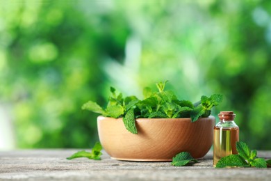 Photo of Bottle of mint essential oil and fresh leaves on wooden table