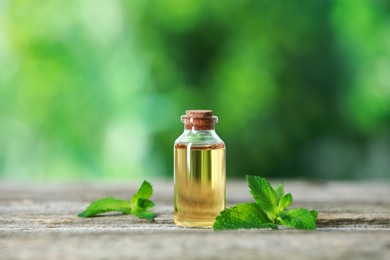 Photo of Bottle of mint essential oil and fresh leaves on wooden table