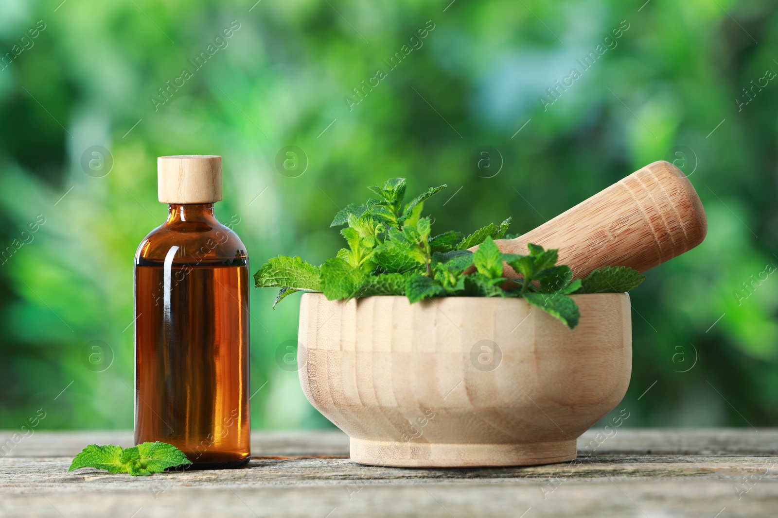 Photo of Bottle of mint essential oil and fresh leaves on wooden table