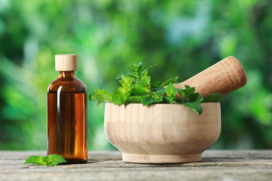 Bottle of mint essential oil and fresh leaves on wooden table