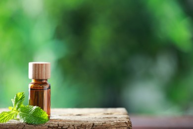 Photo of Bottle of mint essential oil and fresh leaves on wooden table, space for text