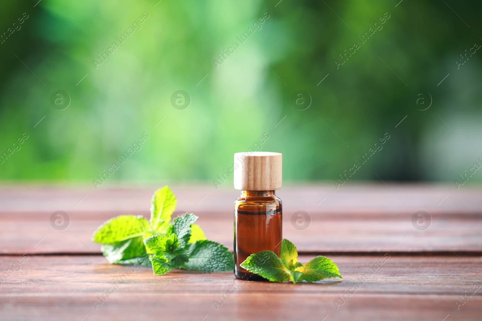 Photo of Bottle of mint essential oil and fresh leaves on wooden table