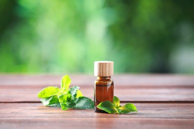 Photo of Bottle of mint essential oil and fresh leaves on wooden table