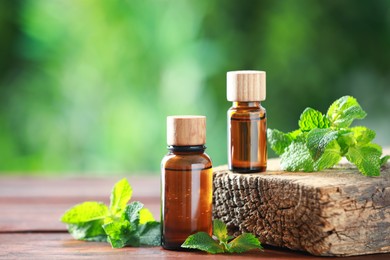 Photo of Bottles of mint essential oil and fresh leaves on wooden table