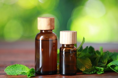 Photo of Bottles of mint essential oil and fresh leaves on wooden table