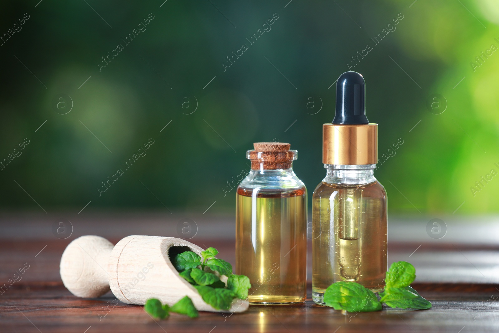 Photo of Bottles of mint essential oil and fresh leaves on wooden table