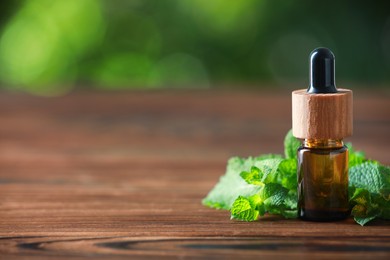 Photo of Bottle of mint essential oil and fresh leaves on wooden table, space for text