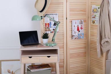 Photo of Folding screen, table, laptop and lamp indoors. Interior design