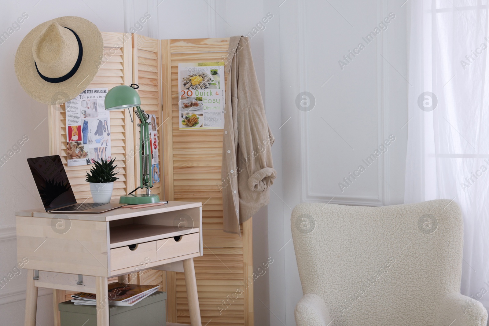 Photo of Folding screen, table, laptop, lamp and armchair indoors. Interior design