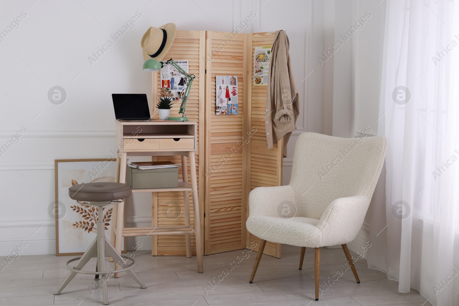 Photo of Folding screen, table, laptop, lamp and armchair indoors. Interior design