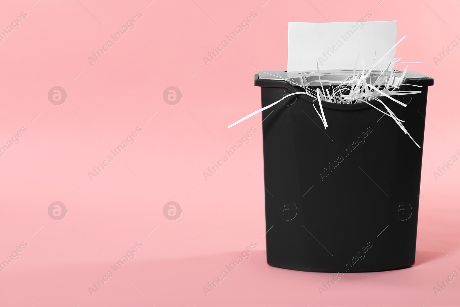 Photo of Destroying sheet of paper with shredder on pink background, space for text