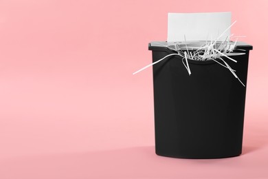 Destroying sheet of paper with shredder on pink background, space for text