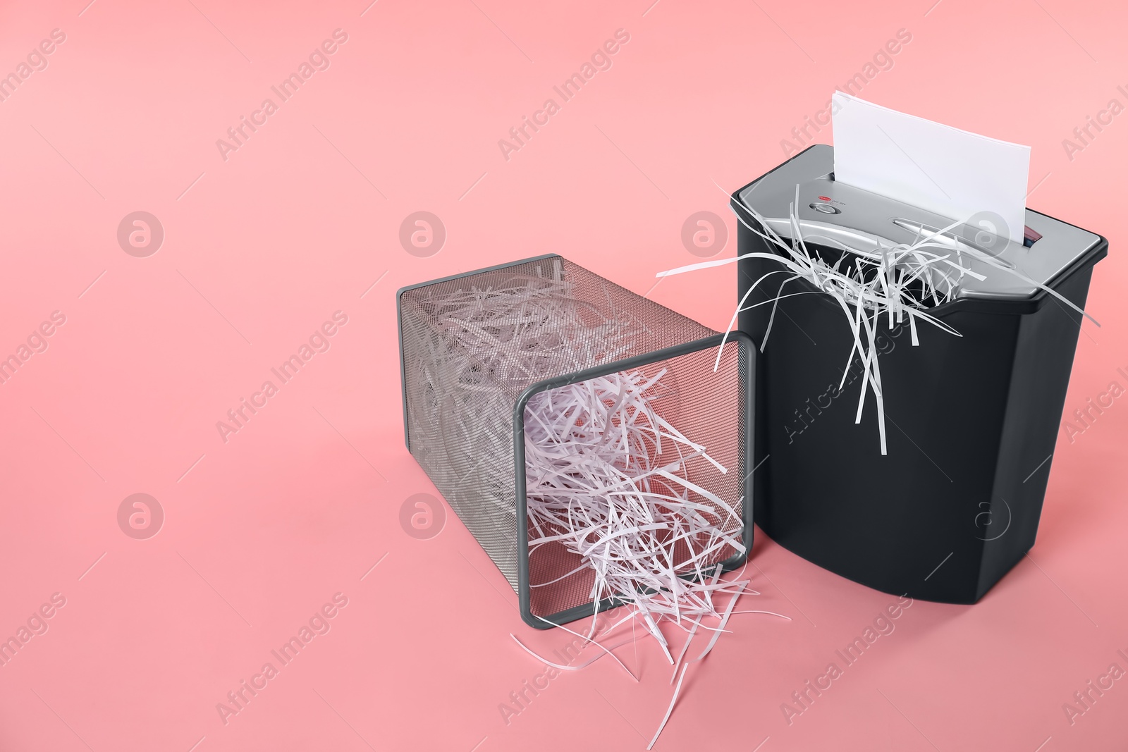 Photo of Shredder, metal basket and paper strips on pink background, space for text