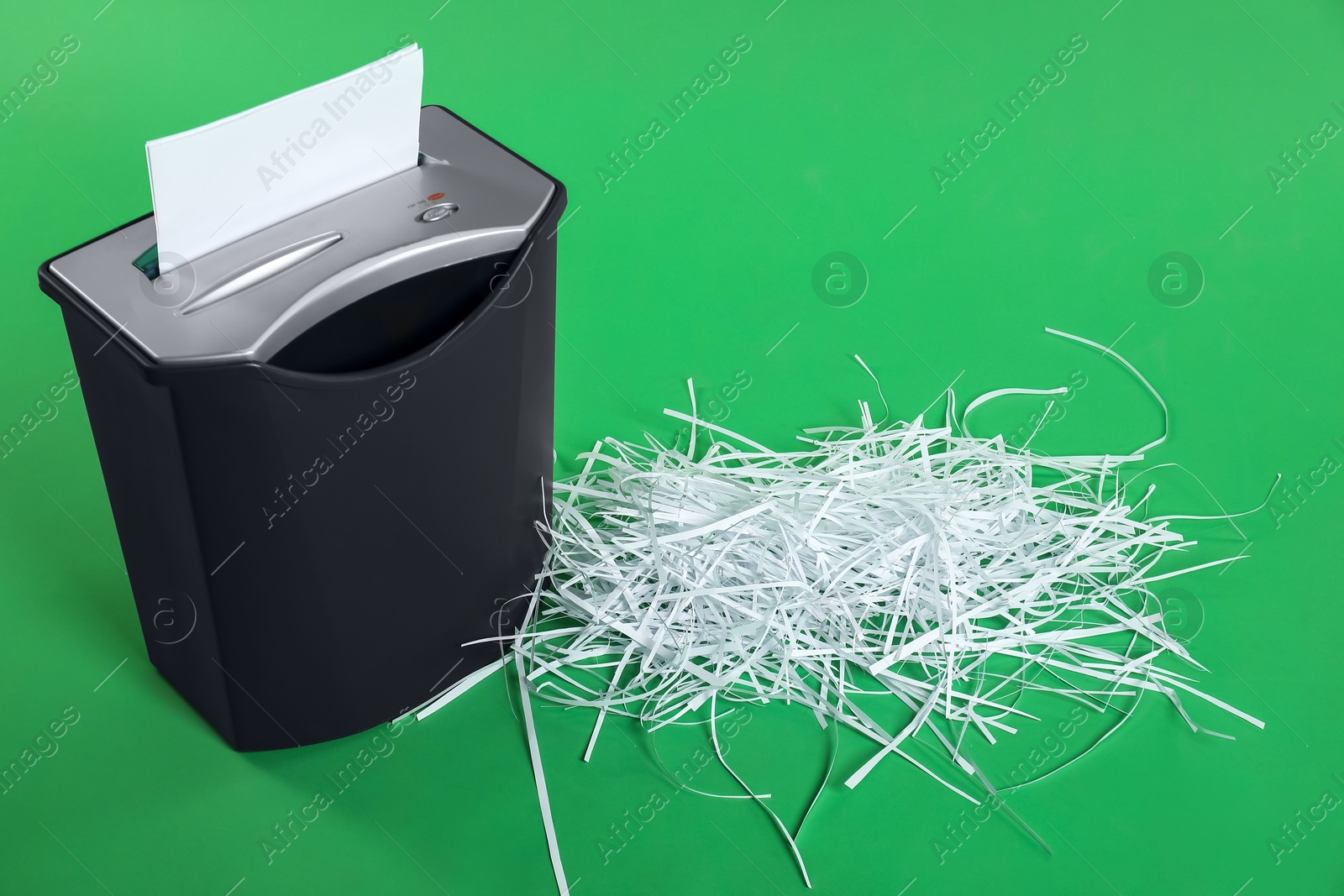 Photo of Shredder and pile of paper strips on green background