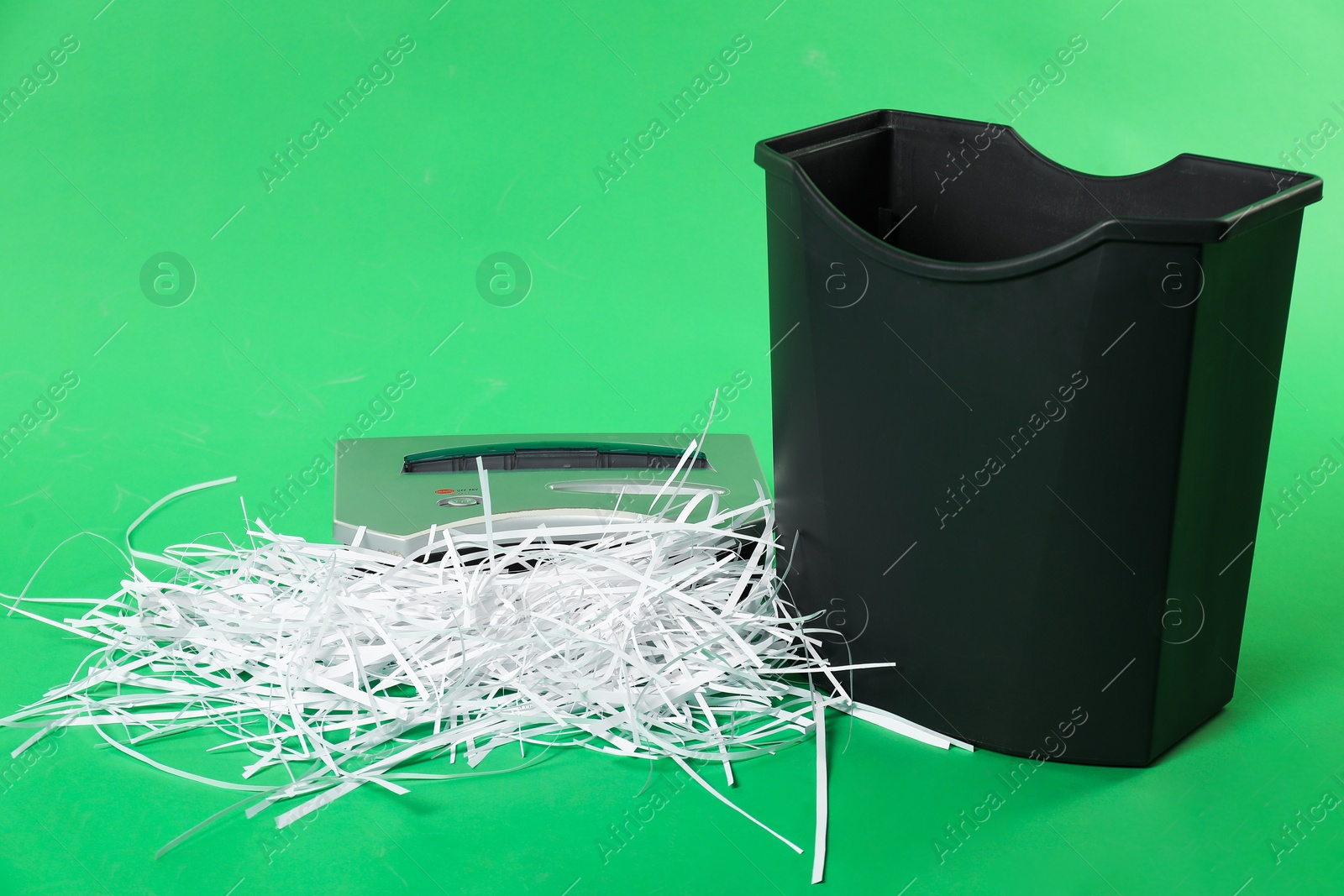 Photo of Shredder, basket and paper strips on green background