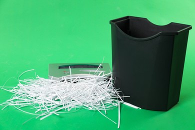 Photo of Shredder, basket and paper strips on green background