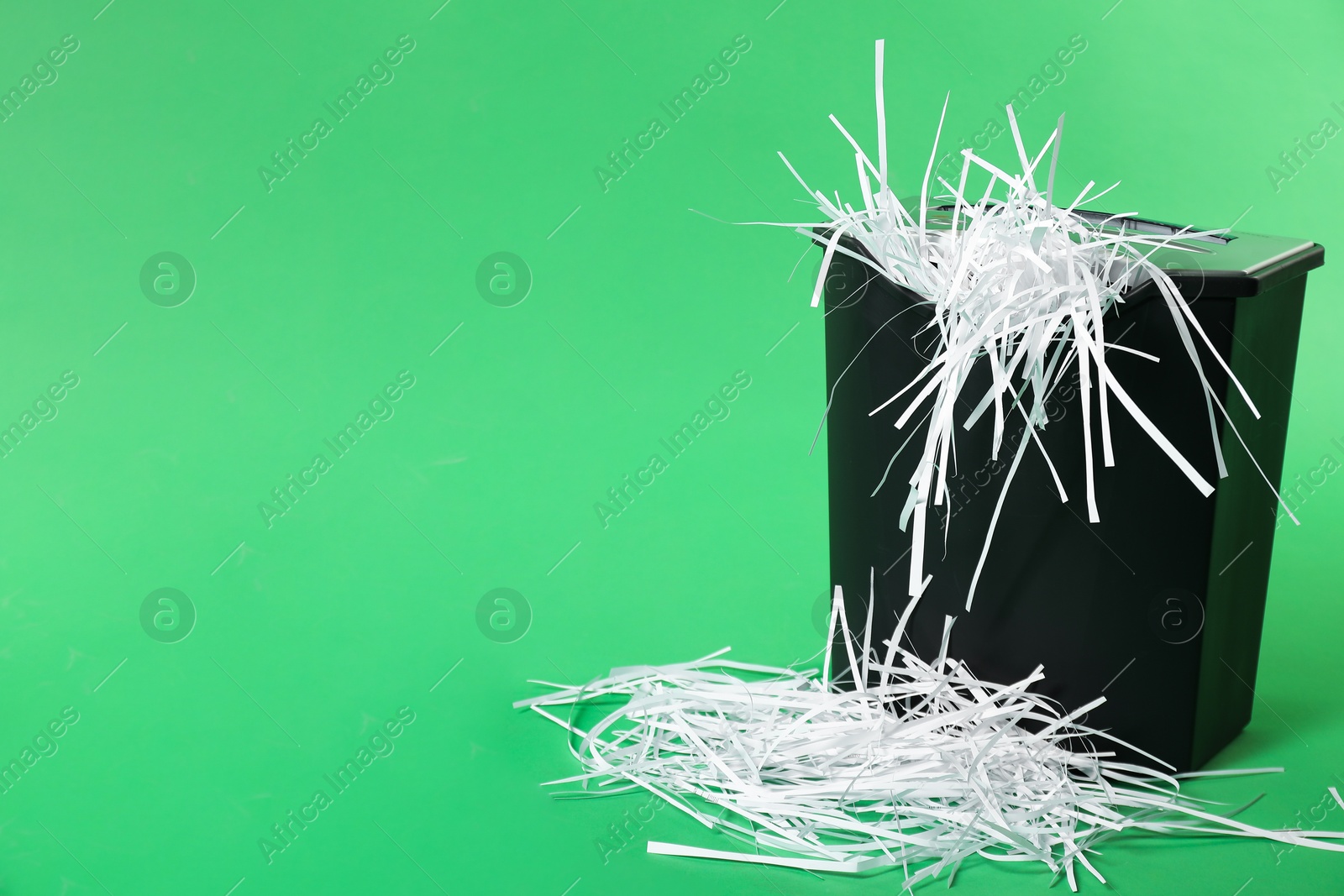 Photo of Basket and shredded paper strips on green background, space for text