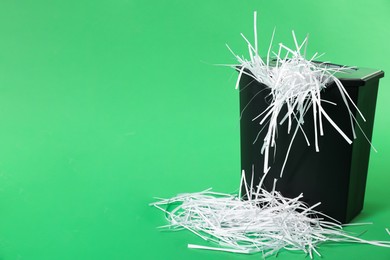 Photo of Basket and shredded paper strips on green background, space for text