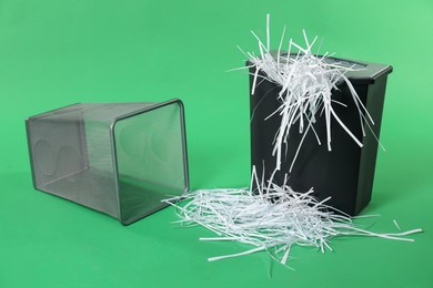 Shredder, metal basket and paper strips on green background