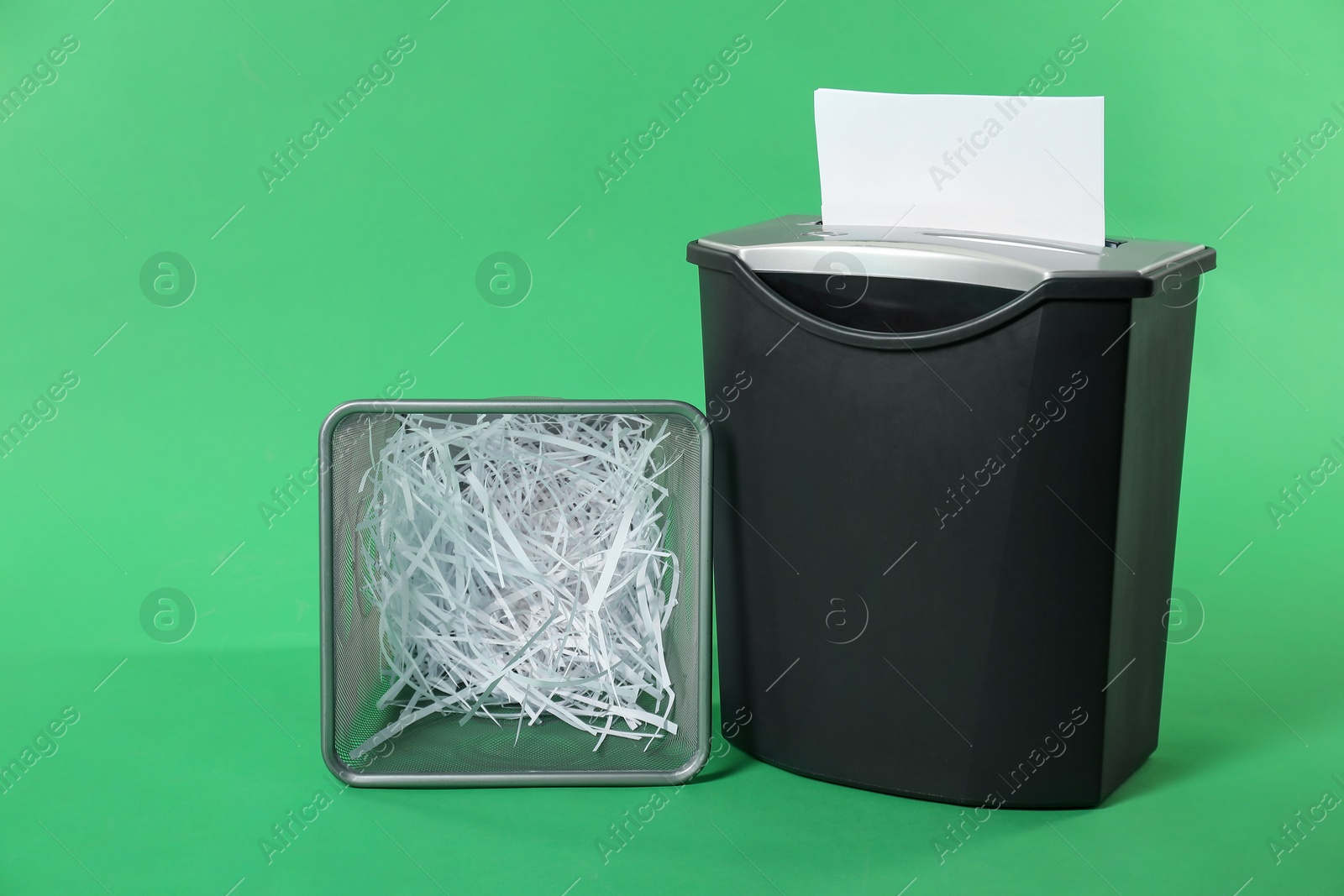 Photo of Shredder, metal basket and paper strips on green background