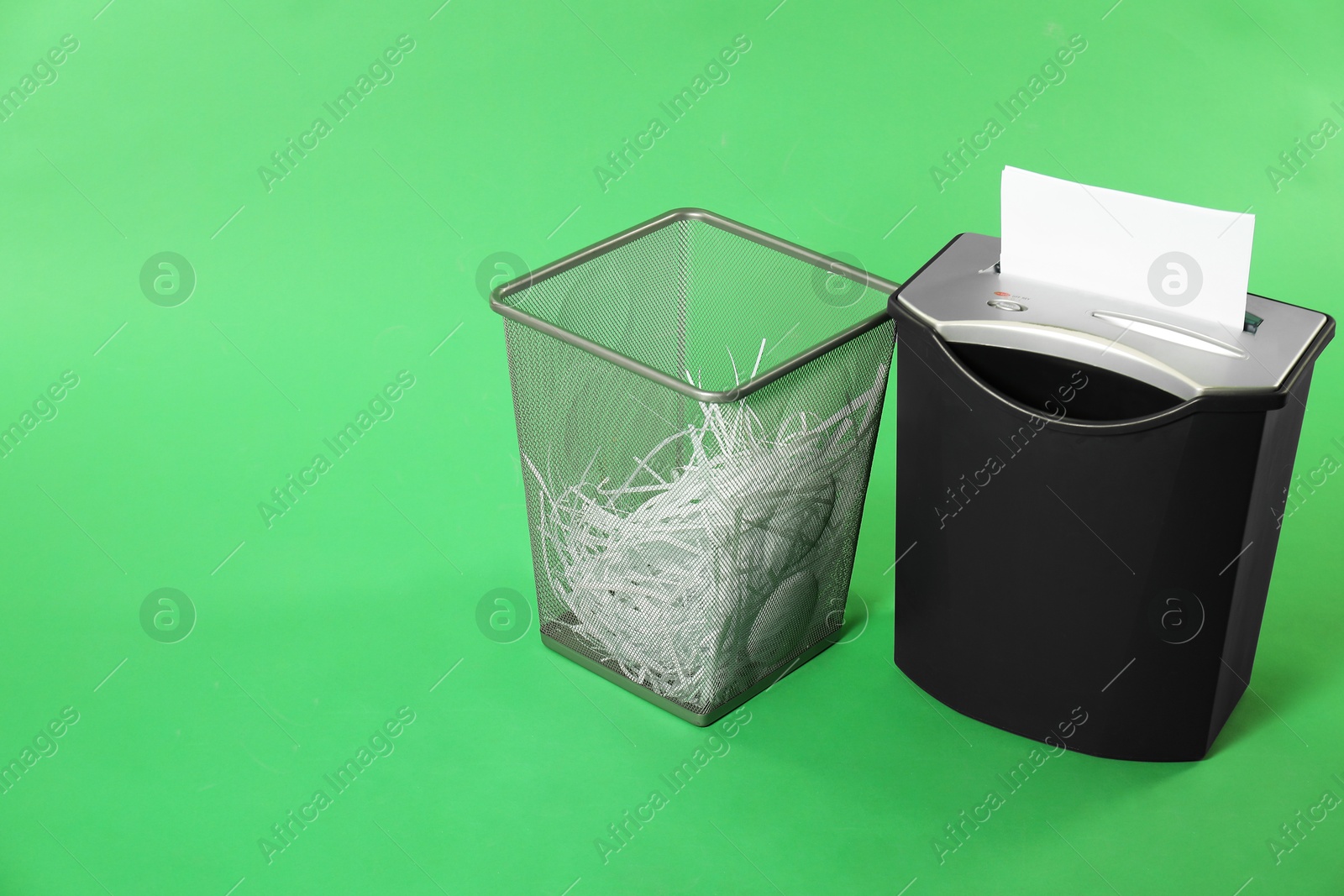 Photo of Shredder, metal basket and paper strips on green background, space for text