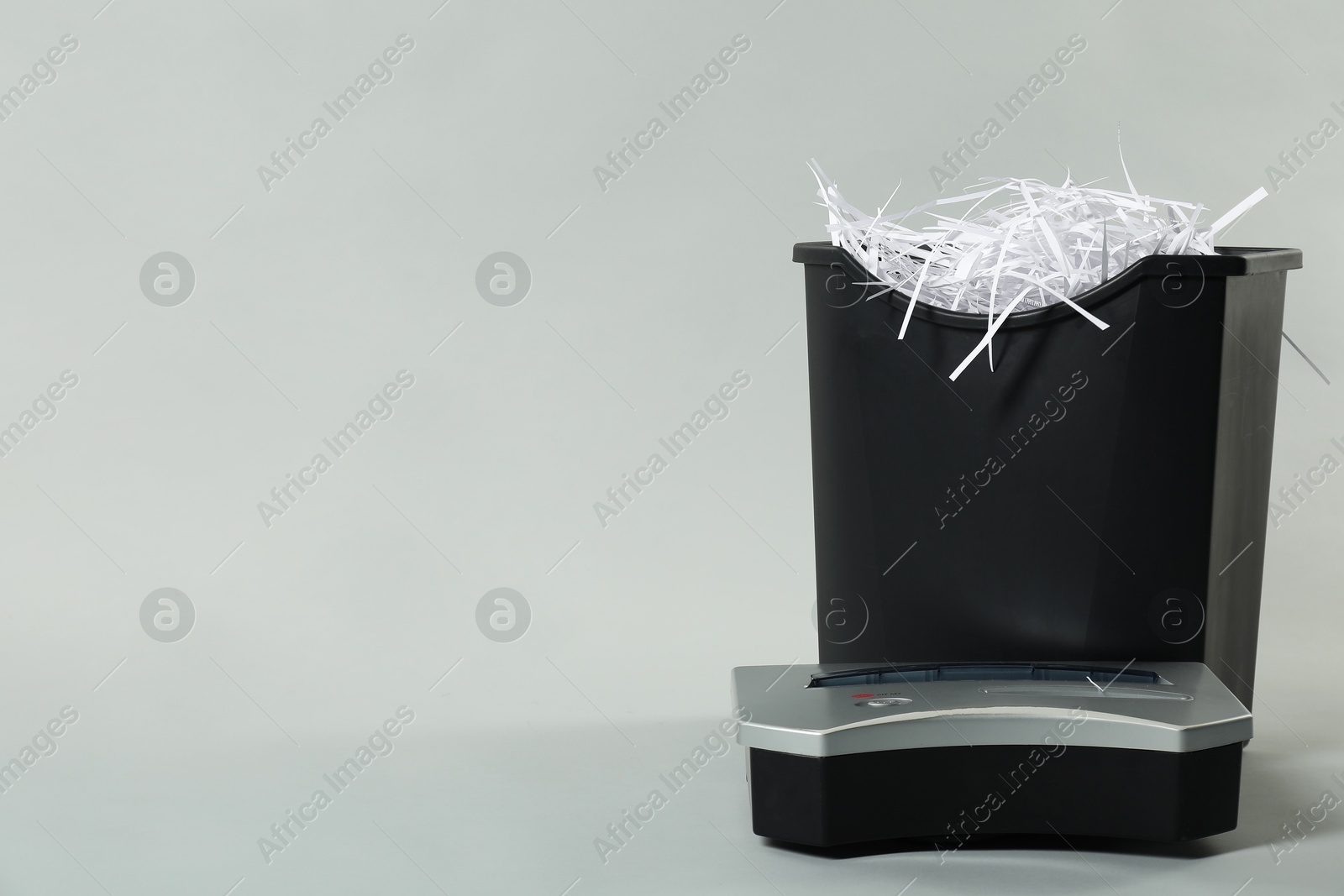 Photo of Shredder, basket and paper strips on light grey background, space for text