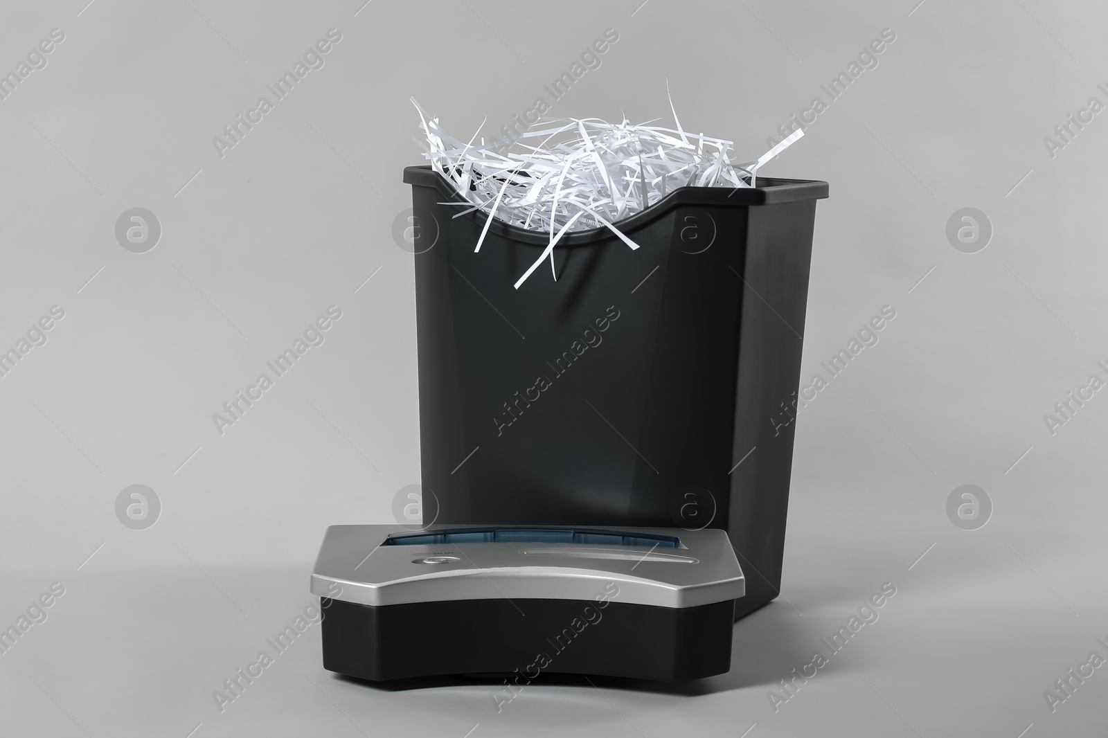 Photo of Shredder, basket and paper strips on light grey background