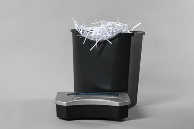 Shredder, basket and paper strips on light grey background