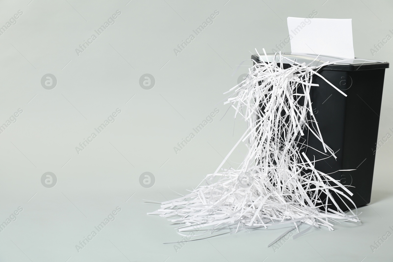 Photo of Destroying sheet of paper with shredder on light grey background, space for text