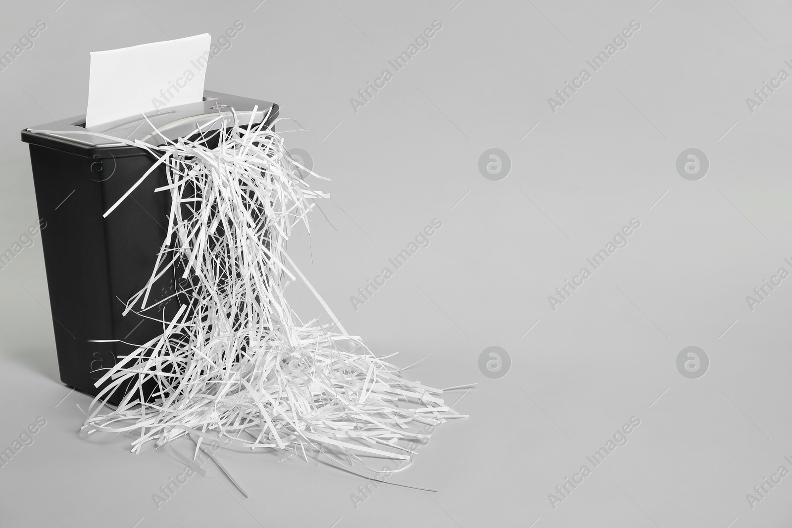 Photo of Destroying sheet of paper with shredder on light grey background, space for text