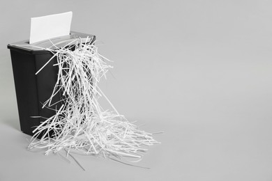 Photo of Destroying sheet of paper with shredder on light grey background, space for text