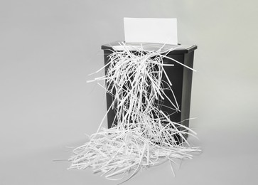 Photo of Destroying sheet of paper with shredder on light grey background, space for text