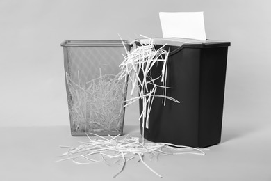 Photo of Shredder, metal basket and paper strips on light grey background