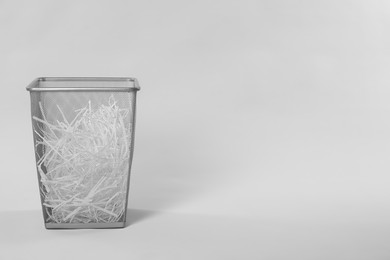 Photo of Shredded paper strips in trash bin on light grey background, space for text