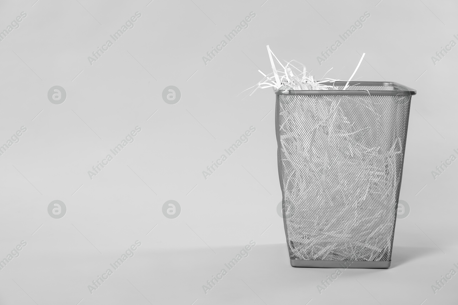 Photo of Shredded paper strips in trash bin on light grey background, space for text