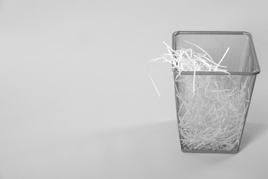 Photo of Shredded paper strips in trash bin on light grey background, space for text