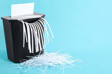 Photo of Destroying sheet of paper with shredder on light blue background, space for text