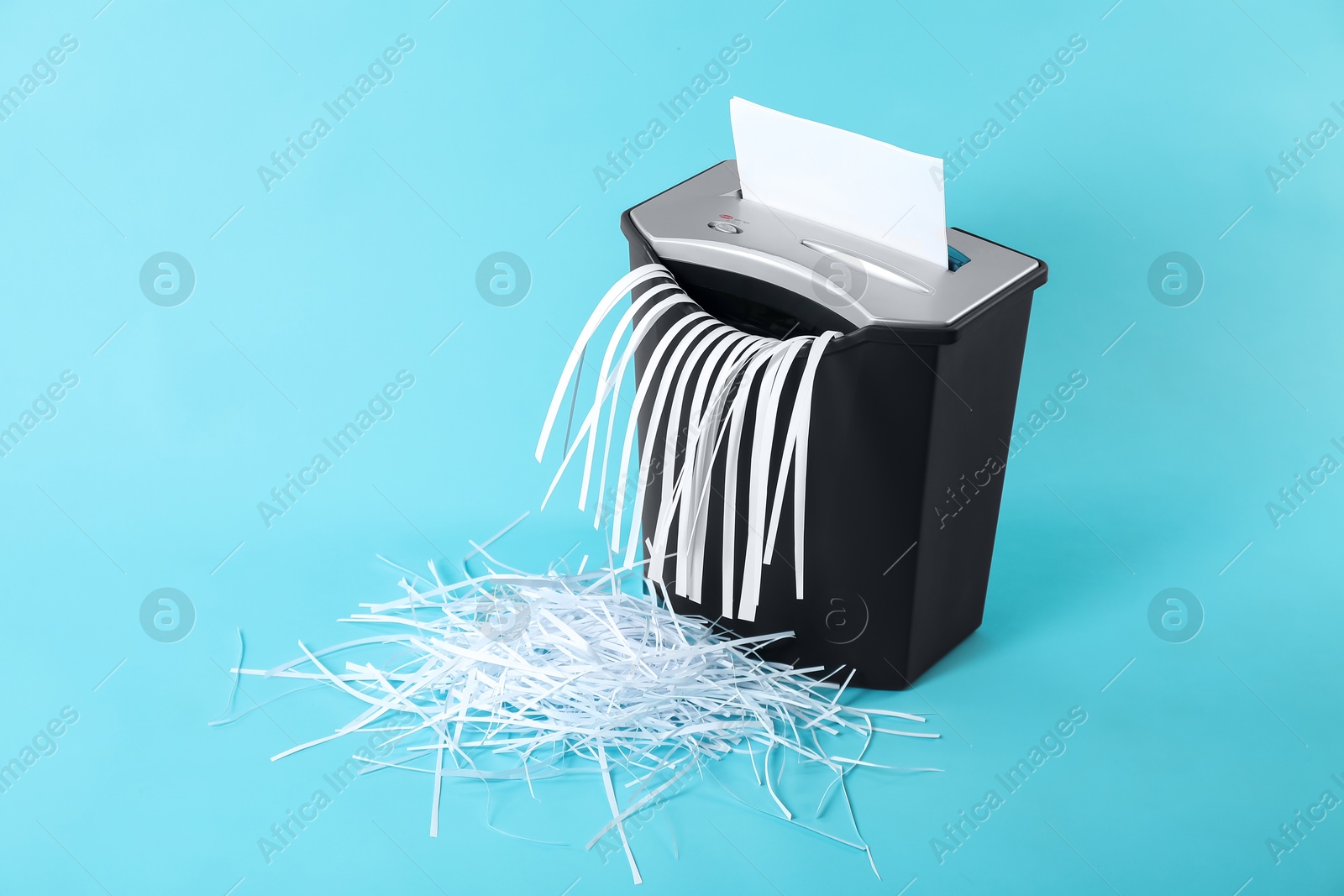 Photo of Destroying sheet of paper with shredder on light blue background