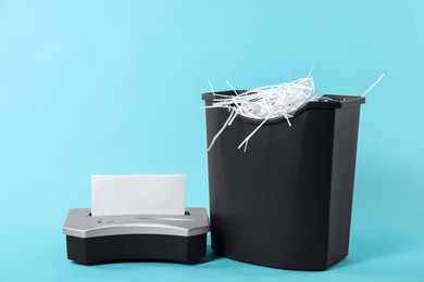 Photo of Shredder, basket and paper strips on light blue background